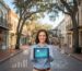 Vibrant scene of DeLand downtown with business owner holding tablet displaying digital growth analytics, blending local charm and modern marketing.