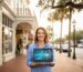 Smiling small business owner in front of Deland storefront holding laptop with SEO growth visuals.