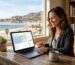 Smiling small business owner working at a wooden desk in a sunlit Ventura office, viewing an AI local SEO dashboard on a laptop with maps and graphs, Ventura Pier visible through the window.