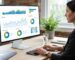 A digital marketer working at a desk with a monitor showing a data dashboard with charts and graphs, representing GA4 reporting integration.