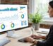 A digital marketer working at a desk with a monitor showing a data dashboard with charts and graphs, representing GA4 reporting integration.
