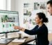 Web designer presenting a custom Shopify ecommerce theme to a colleague on a large monitor in a bright modern office.